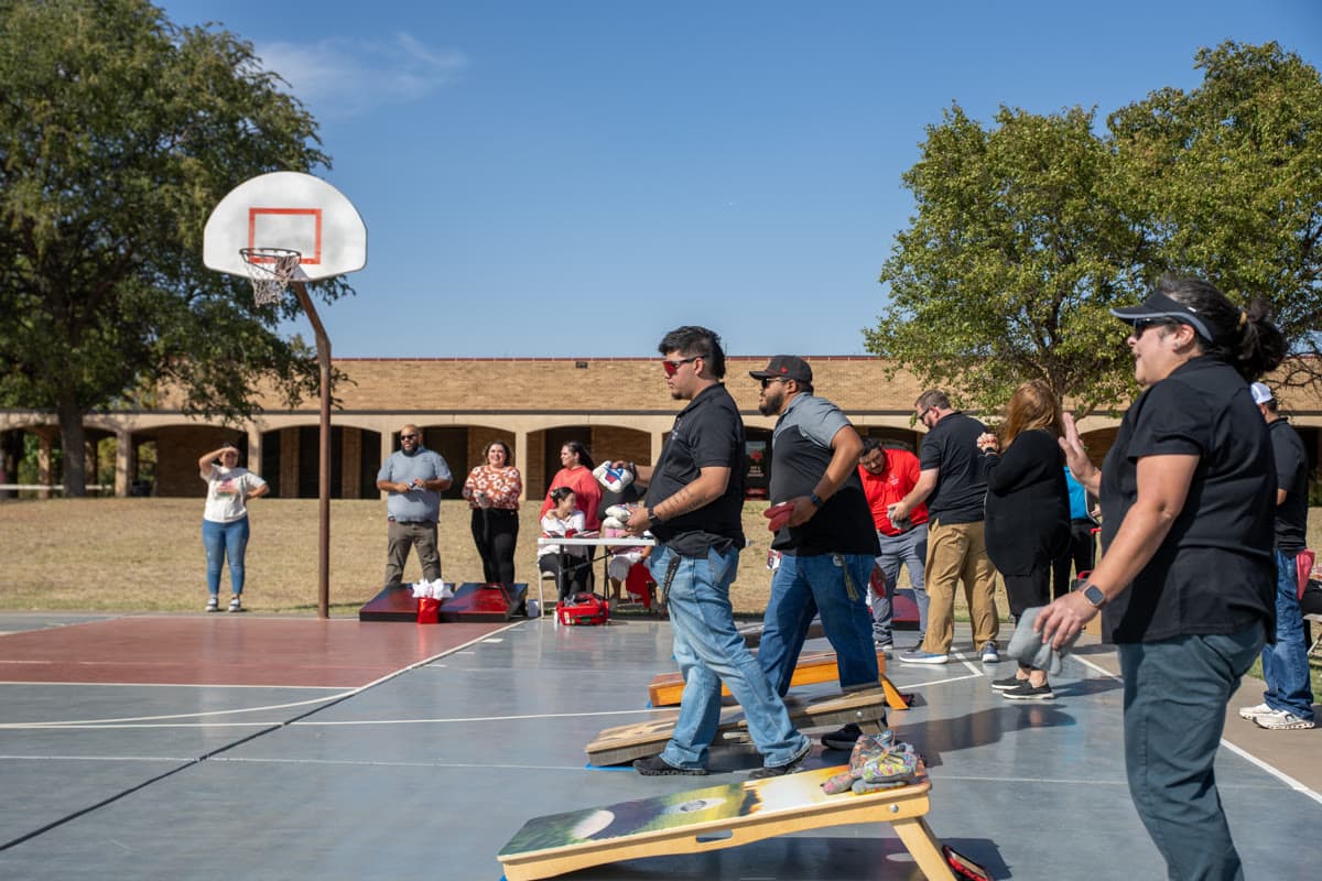 Competitors throw cornhole bags during an outdoor tournament on regulation boards