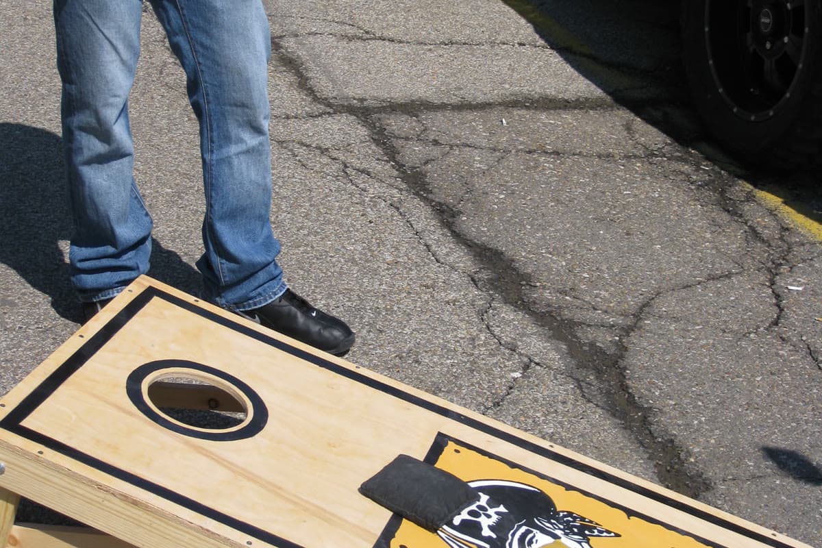Regulation cornhole board with a bold black border stripe and high-contrast graphic on a plywood face at a tailgate