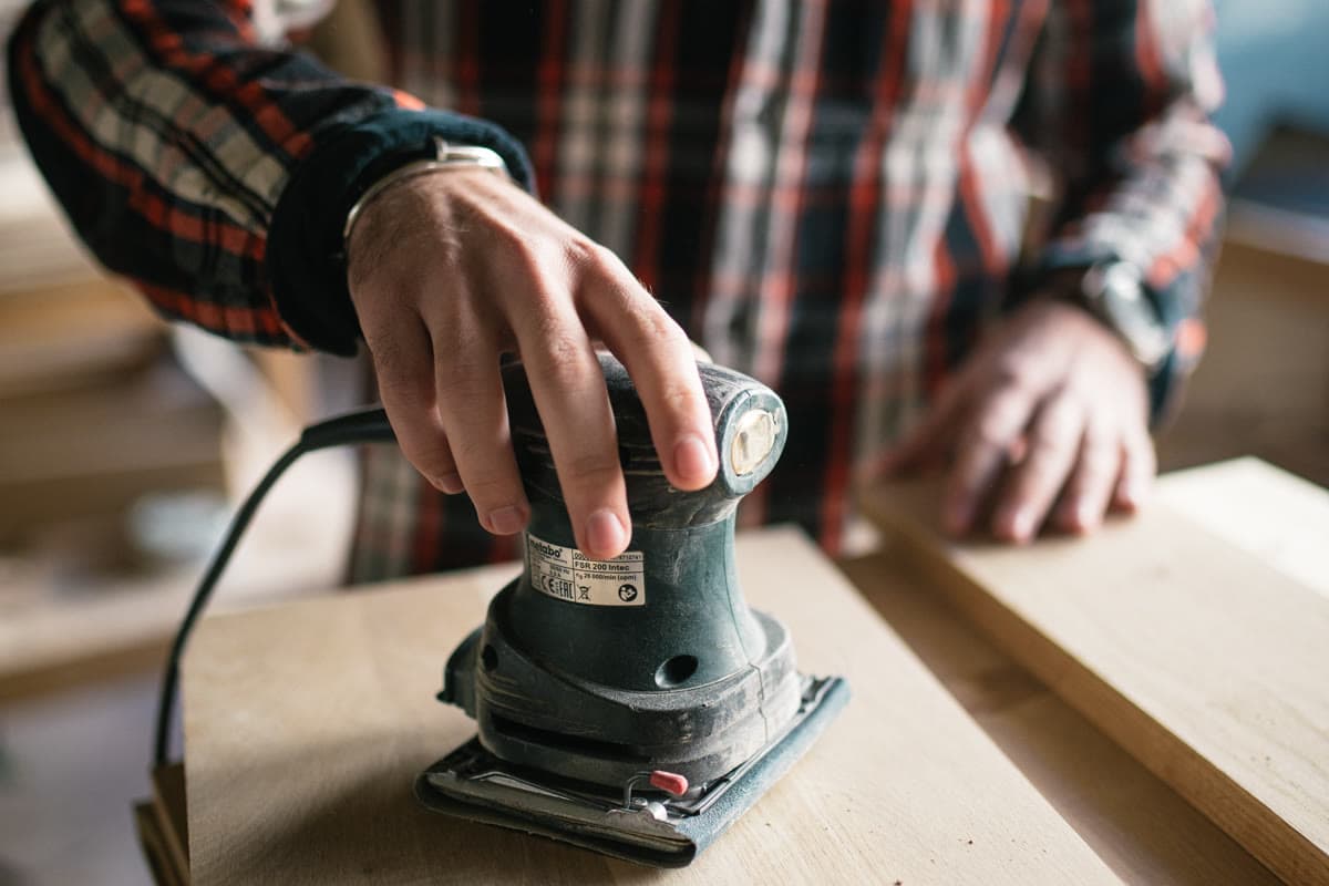 Carpenter sands wooden boards smooth with an electric sander in a workshop before applying an outdoor sealer