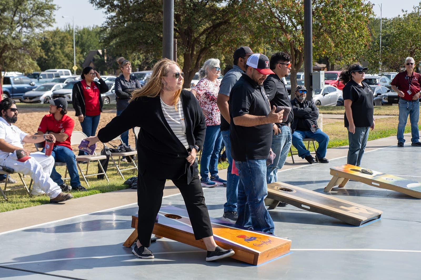 A player throwing a bag at a printed cornhole board during an outdoor tournament