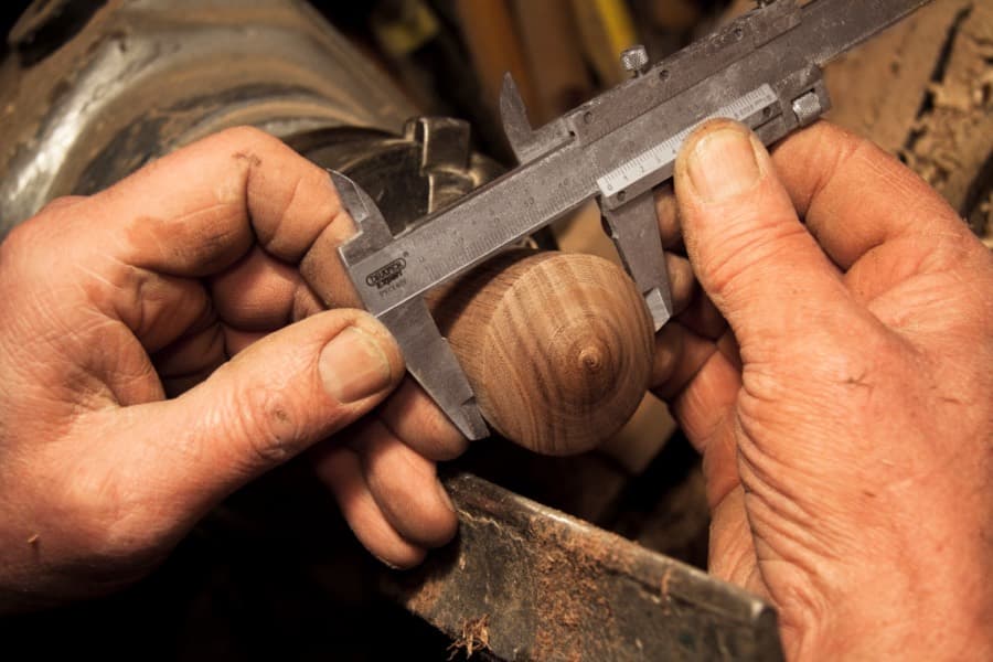 A woodworker checking a piece of turned wood with calipers on a workbench