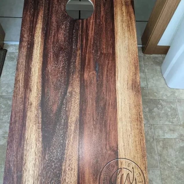 Dark live-edge wood-grain cornhole board with a circular hole and a faint round mark near the bottom