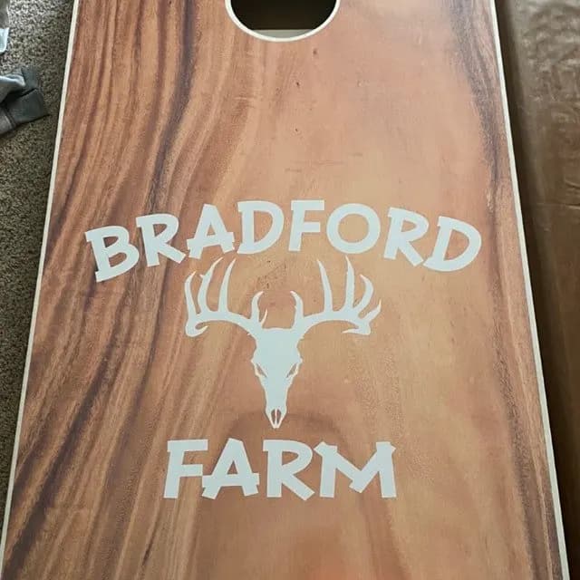 Warm wood-grain cornhole board printed in white with Bradford, a deer skull, and Farm