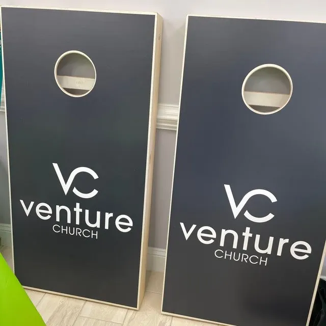 Pair of charcoal cornhole boards printed in white with a VC mark and Venture Church