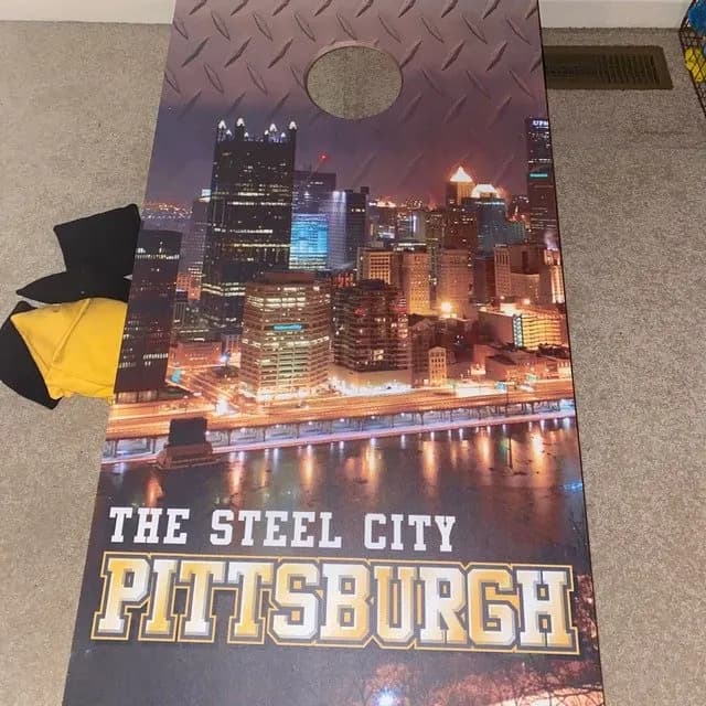Cornhole board printed with a night city skyline, diamond-plate texture near the hole, and The Steel City Pittsburgh