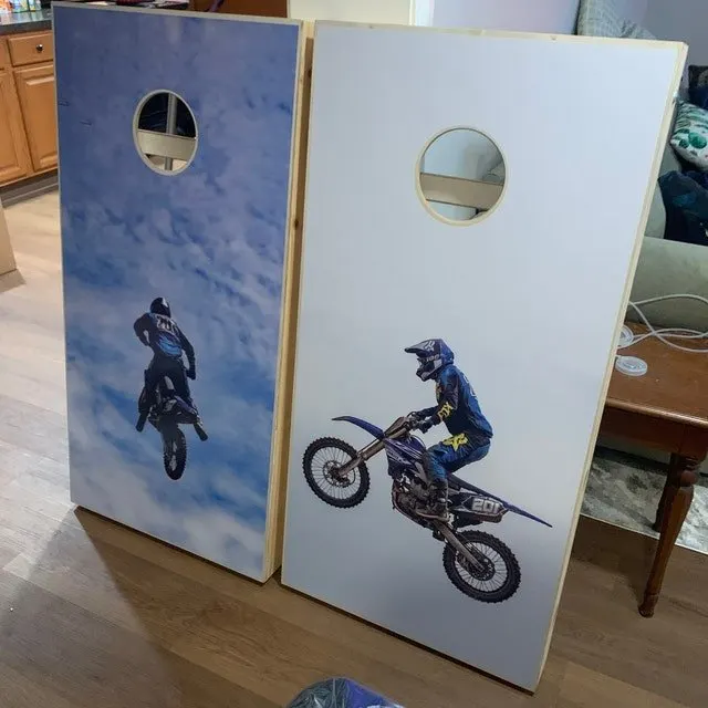 Pair of cornhole boards printed with motocross riders, one against a blue sky and one on a white field