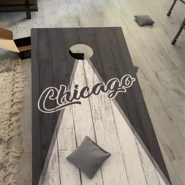 Two-tone gray and white plank cornhole board printed with Chicago in script and a gray bag on the face