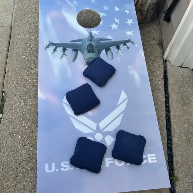 Cornhole board printed with a fighter jet, stars, and a U.S. Air Force mark, with four navy bags on the face