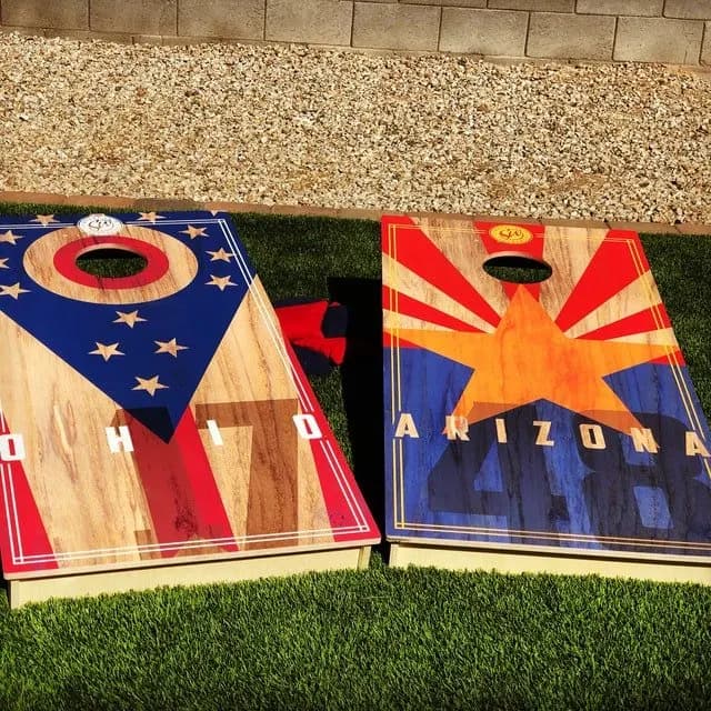 Pair of cornhole boards on turf printed with an Ohio stars-and-stripes layout and an Arizona starburst flag