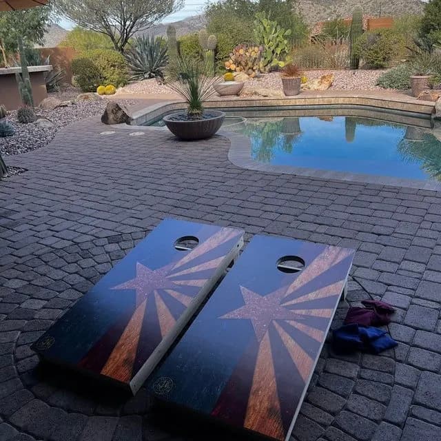 Pair of Arizona-flag star cornhole boards on a paver patio beside a pool, with bags on the ground