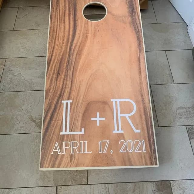 Warm wood-grain cornhole board on tile printed with L + R and April 17, 2021 in white