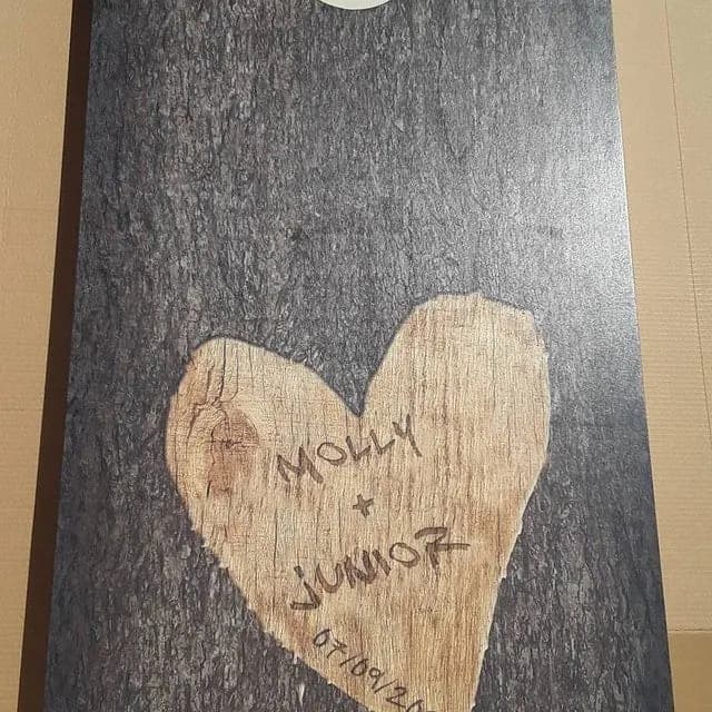 Dark textured cornhole board with a natural wood heart holding handwritten names and a date