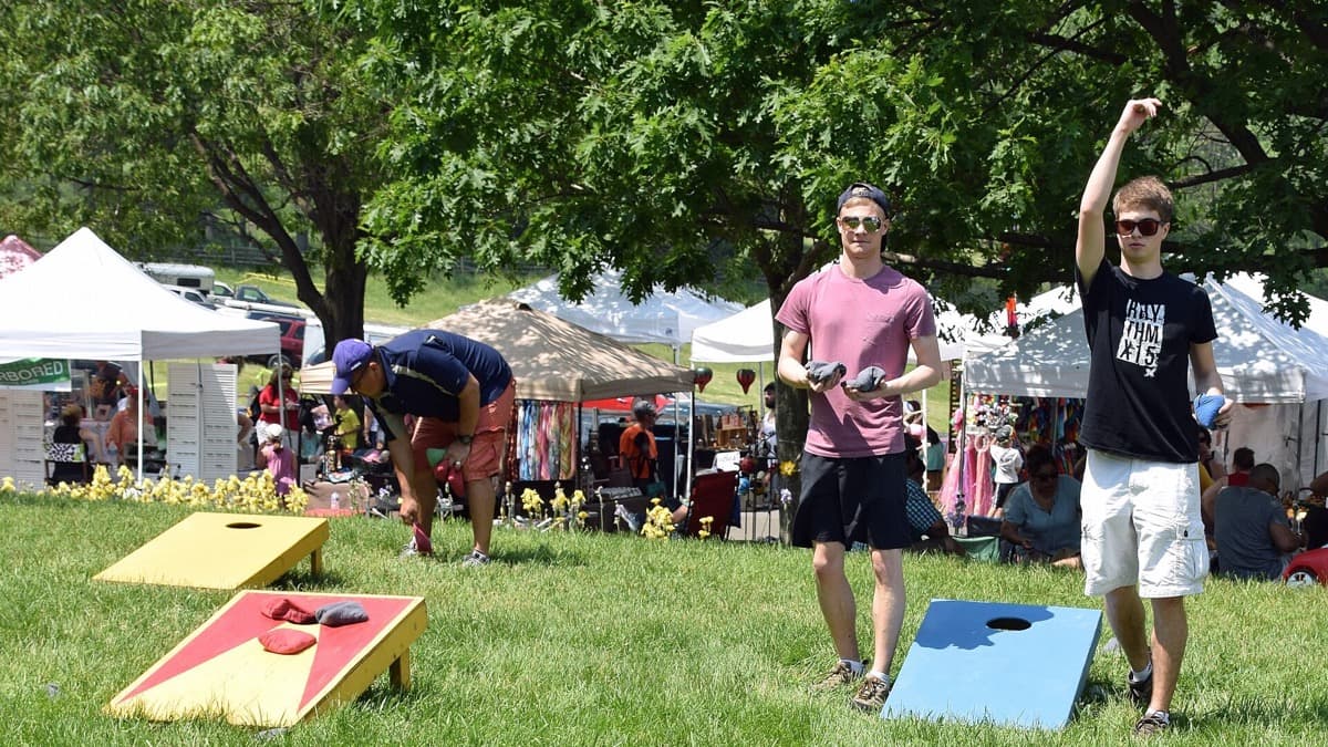 Players toss cornhole bags at a casual outdoor festival game on grass